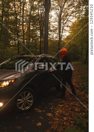 Autumn SUV with Driver with Pumpkin Head in Forest Autumn SUV with Driver with Pumpkin Head in Forest 129345210