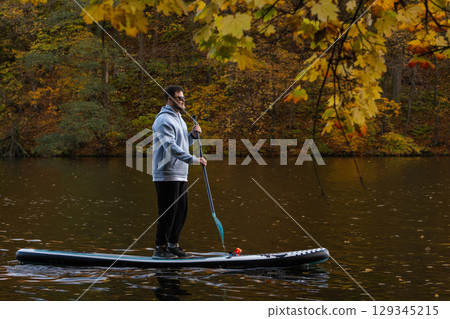 Man Paddleboarding in Autumn Lake 129345215