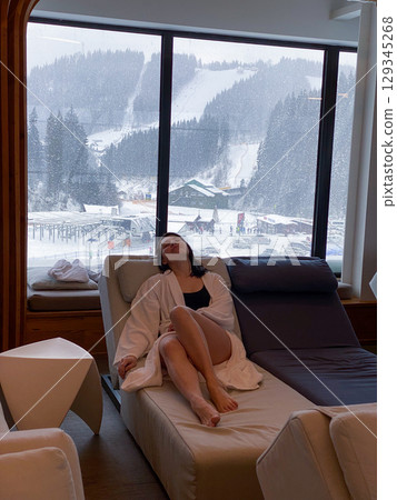 Woman Relaxing Indoors with Snowy Mountain View Woman Relaxing Indoors with Snowy Mountain View 129345268