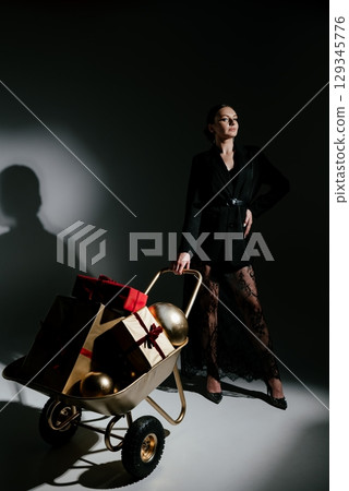 Woman Posing with Gift-Filled Wheelbarrow in Stylish Attire 129345776
