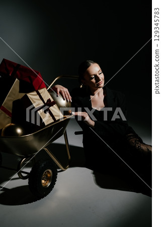 Pensive Woman by Gift Cart with Presents in Dark Setting 129345783