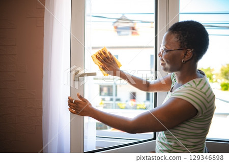 Smiling housekeeper cleaning a window with a yellow cloth 129346898