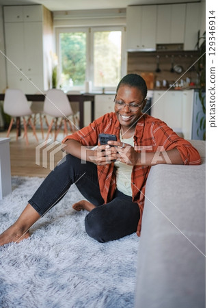 Young black woman using smartphone and smiling at home 129346914