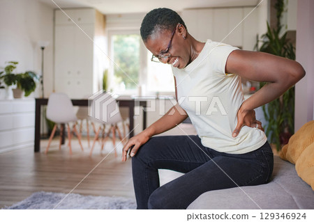 Young woman sitting on sofa at home suffering from back pain 129346924