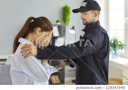 Police officer comforting emotional woman during home visit 129347046