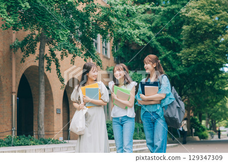 Three university students walking and talking on campus 129347309