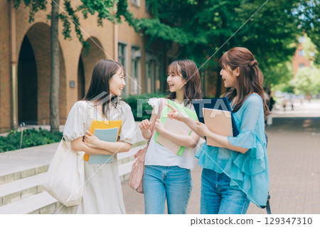 Three university students walking and talking on campus 129347310