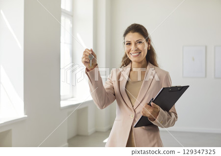 Happy successful realtor, smiling female real estate agent holding keys carrying clipboard  129347325