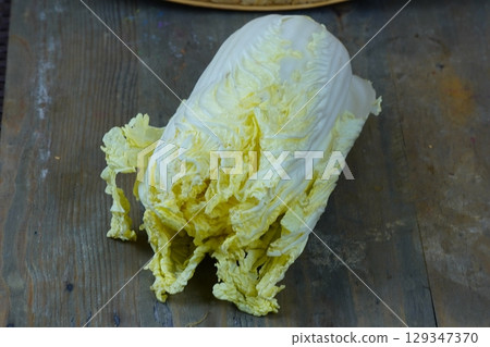 A fresh napa cabbage rests on a rustic wooden table. 129347370