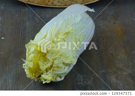 A fresh napa cabbage rests on a rustic wooden table. 129347371