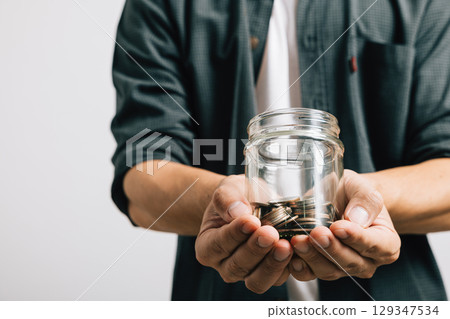 Close up hand of businessman holding a jar full of coins and the coins are in his palm studio shot isolated white background, Money saving and investing or donate money concept Close up hand of businessman holding a jar full of coins and the coins are in his palm studio shot isolated white background, Money saving and investing or donate money concept 129347534