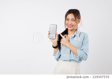 A happy Asian woman holding a mobile phone in her hand, pointing to the blank screen. She is excited, showing the smart phone display. isolated studio white background A happy Asian woman holding a mobile phone in her hand, pointing to the blank screen. She is excited, showing the smart phone display. isolated studio white background 129347535