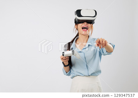 VR game moment where Young woman in headset plays VR game using controller and points or touch into virtual reality imaginary panel with joy. isolated studio white background VR game moment where Young woman in headset plays VR game using controller and points or touch into virtual reality imaginary panel with joy. isolated studio white background 129347537
