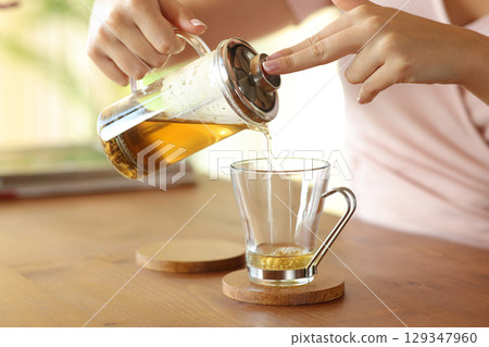 Woman hand pouring tea from infuser in a glass 129347960