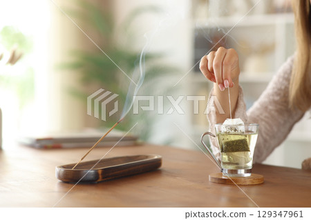 Woman hand preparing tea beside incense stick burning at home 129347961