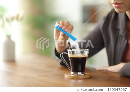 Woman hand throwing sugar in a coffee cup on a table at home Woman hand throwing sugar in a coffee cup on a table at home 129347967