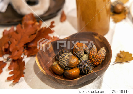 Autumn table decoration with wooden bowl chestnuts, pine cones and oak leaves on table Autumn table decoration with wooden bowl chestnuts, pine cones and oak leaves on table 129348314