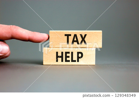 Tax help symbol. Concept words Tax help on wooden blocks on a beautiful grey table grey background. Businessman hand. Business, support and tax help concept. Copy space. Tax help symbol. Concept words Tax help on wooden blocks on a beautiful grey table grey background. Businessman hand. Business, support and tax help concept. Copy space. 129348349