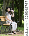 A young woman sitting on a bench in the shade of a tree and drinking water from her own bottle 129348767