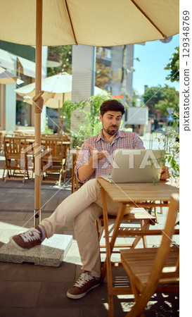 Businessman talking during video call while sitting at cafe on a summer terrace. 129348769
