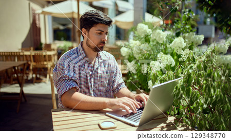 Business man working on laptop sitting at cafe table outdoors 129348770