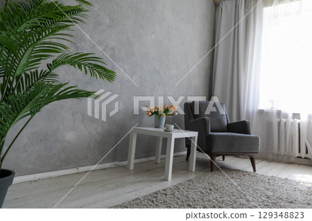 Armchair and table with a vase of flowers in the interior of a room 129348823