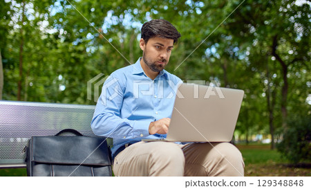 Man concentrating on laptop screen while working remotely in park 129348848