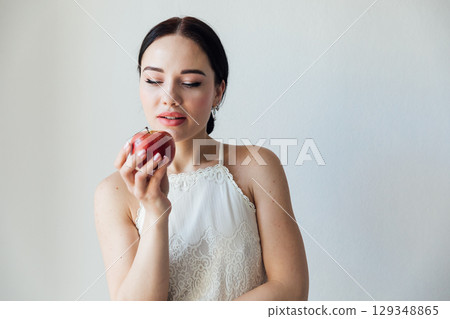 woman in a white dress holding a red apple in her hands for food on a diet 129348865