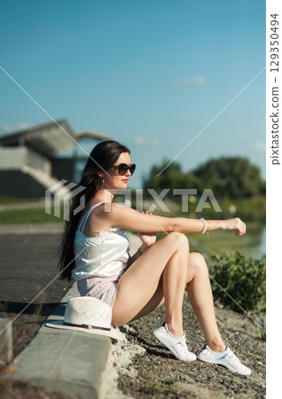 A girl in shorts and a T-shirt sits on the grass, basking in the sun 129350494