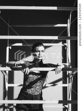 A slender girl in a light-colored outfit poses near the scaffolding A slender girl in a light-colored outfit poses near the scaffolding 129350504
