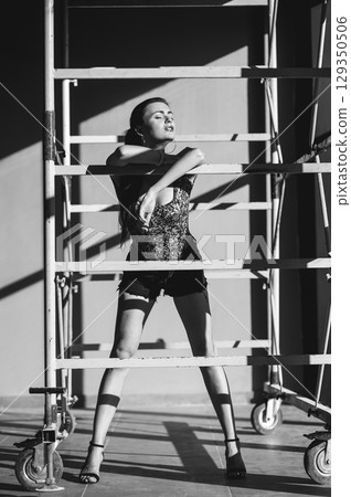 A brave girl stands near a scaffolding in a sporty style A brave girl stands near a scaffolding in a sporty style 129350506