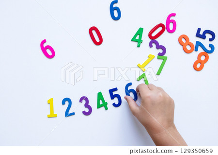 Child hand arranging colorful numbers on white background Child hand arranging colorful numbers on white background 129350659