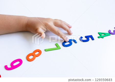 Child hand reaching for colorful numbers on white background 129350683
