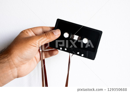 Hand holding vintage black cassette tape with unraveled magnetic tape 129350688
