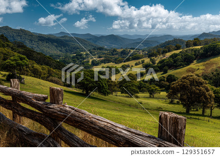 Rustic wooden fence along a green pasture beneath blue sky 129351657
