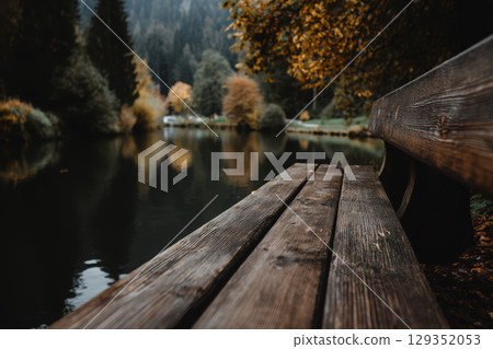 Rustic wooden bench overlooking serene autumn lake 129352053