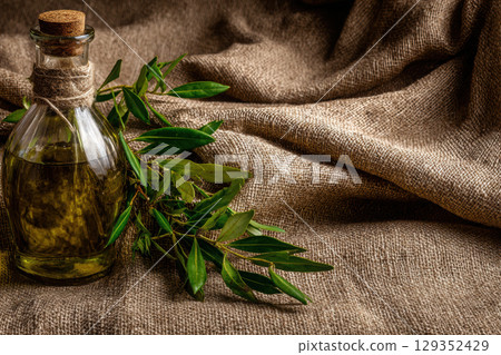 Rustic olive oil bottle and branches on natural linen cloth 129352429
