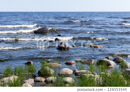 Green grass grows on a rocky coast as lake waves gently break Green grass grows on a rocky coast as lake waves gently break 129353545