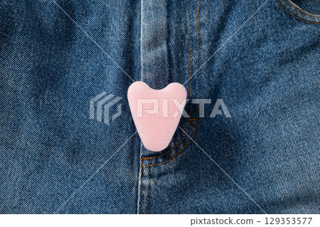Female pink foam tampon stringless as heart on jeans. New generation. Hygiene accessories for women. View from above. 129353577