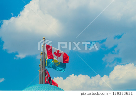 National flags of countries: Canada, Kazakhstan, United States, China, mounted on silvery high metal flagpoles, wriggle in wind, stabilized by weights on blue sky background with white fluffy clouds National flags of countries: Canada, Kazakhstan, United States, China, mounted on silvery high metal flagpoles, wriggle in wind, stabilized by weights on blue sky background with white fluffy clouds 129353631