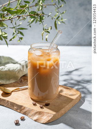 Ice latte coffee in a glass with milk on a wooden board on a light background with branch 129354413