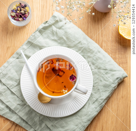 A cup of herbal tea with lemon and bouquet of flowers on a wooden table with napkin. 129354414