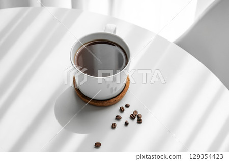 Freshly brewed espresso coffee in a cup on a white table near window with coffee beans  129354423