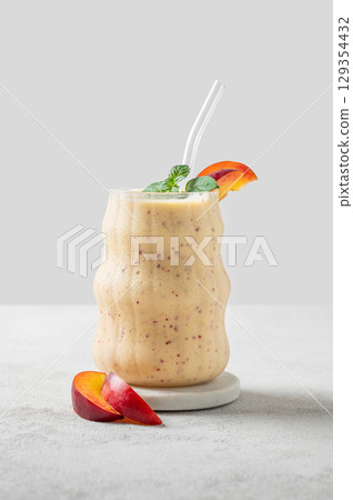 Smoothie with peach and banana in a glass on a marble stand on a light background  129354432