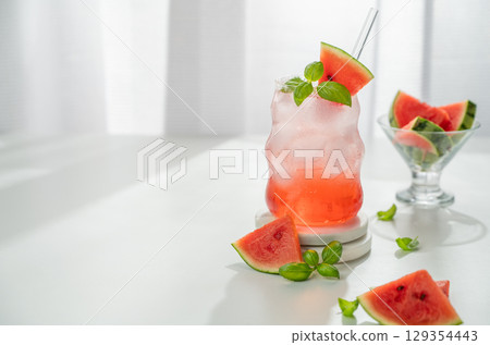 Watermelon mojito cocktail with ice and mint in a glass on a white table near window with slices Watermelon mojito cocktail with ice and mint in a glass on a white table near window with slices 129354443