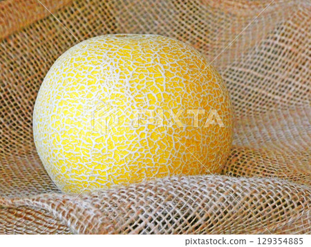 A simple photo of a yellow netted melon with a hemp bag in the background 129354885