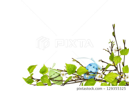 The first spring leaves and small flowers on tree branches with decorative Easter eggs isolated on white 129355325
