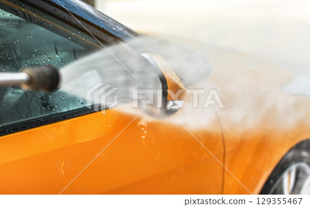 Side mirror of yellow car being washed in self service carwash, water spraying with high pressure, drops flying around. 129355467