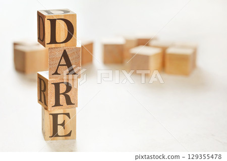 Four wooden cubes arranged in stack with text DARE (meaning Define, Assess, Respond, Evaluate) on them, space for text / image at down right corner 129355478