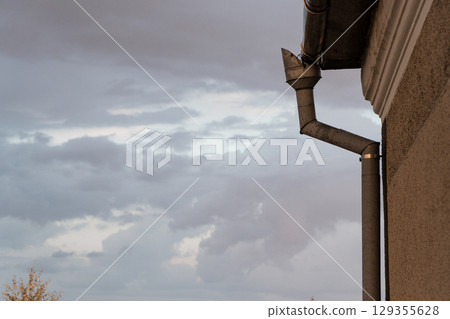 Cloudy Sky Over Gutter Downspout on Textured Beige Building Exterior, Rainwater Drainage System, Grey Stormy Weather Cloudy Sky Over Gutter Downspout on Textured Beige Building Exterior, Rainwater Drainage System, Grey Stormy Weather 129355628